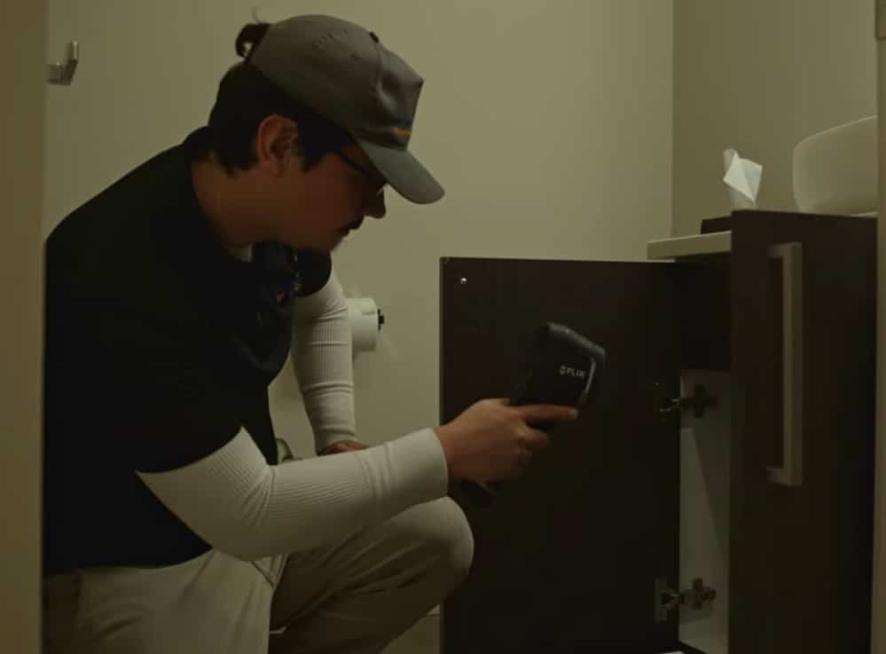 A professional inspector uses a FLIR thermal imaging camera to check inside a bathroom cabinet for hidden moisture during a mold inspection seattle wa.